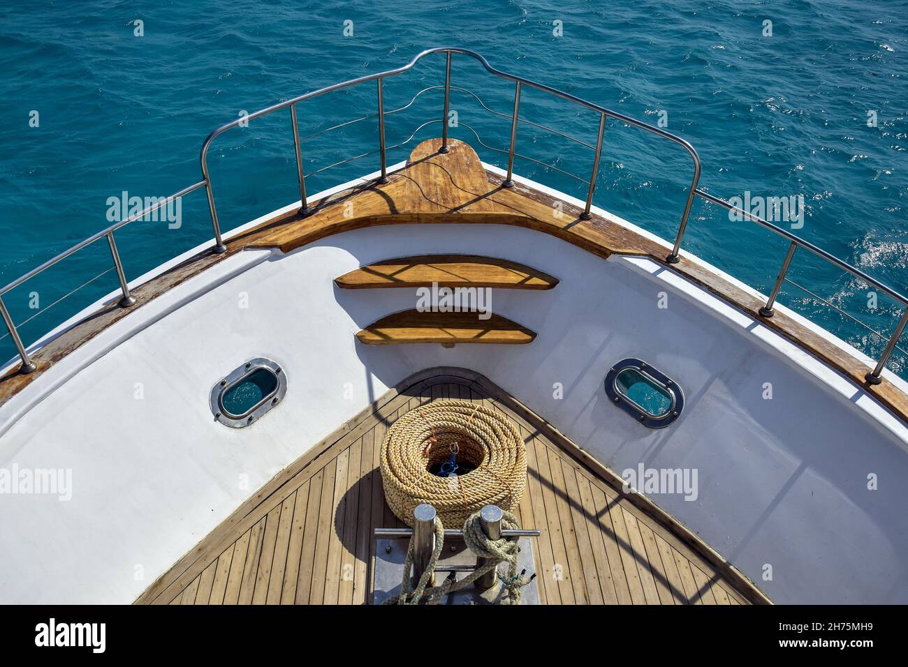 Arc de yacht blanc sur fond de mer bleue.Baie avec une corde épaisse se trouve sur une terrasse en bois.Garde-corps en acier-clôtures.vue de dessus.Gros plan.Mise au point sélective. Banque D'Images