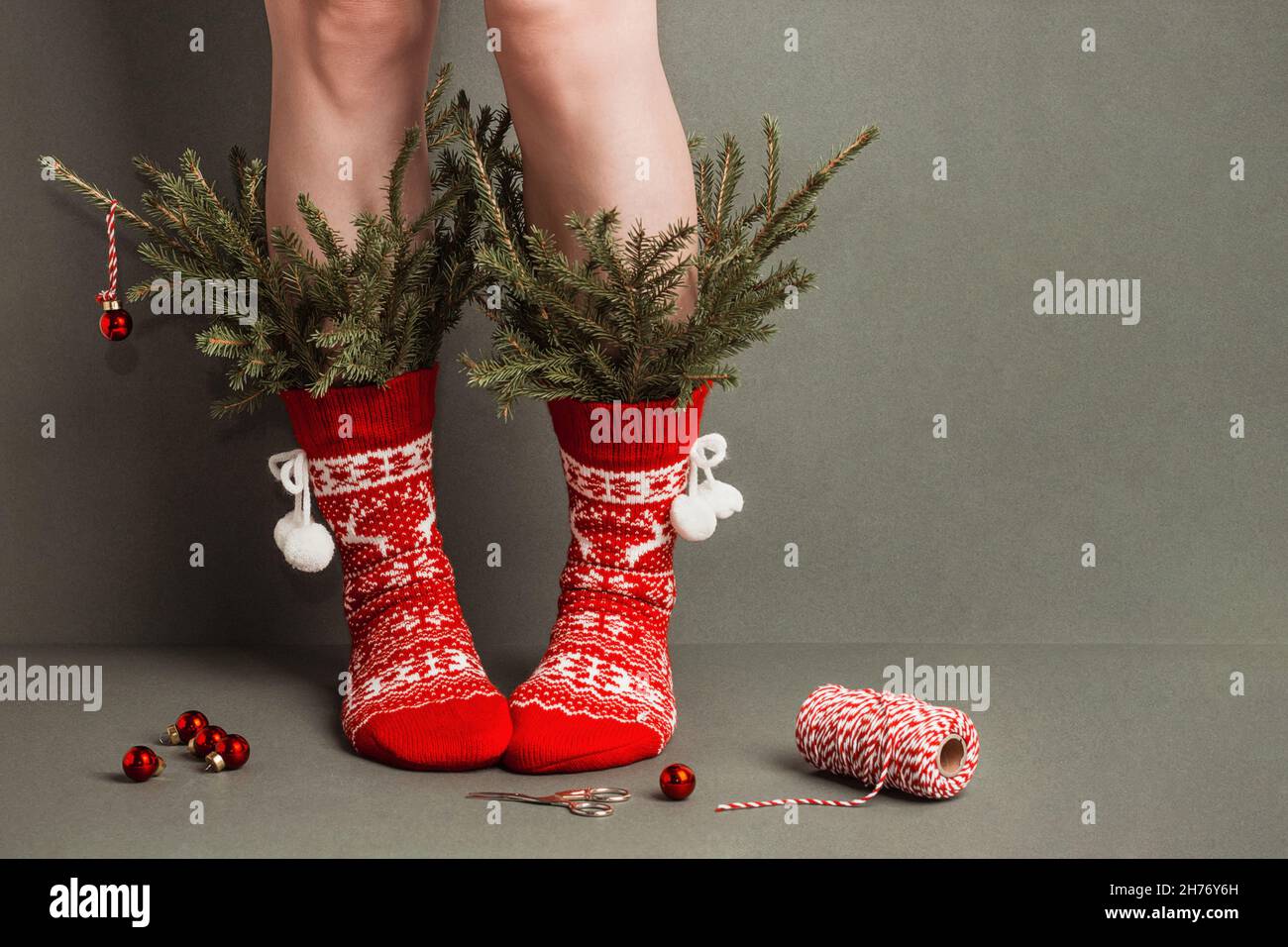 Pattes de femme en chaussettes rouges en laine avec ornements et branches de sapin minimaliste décorées sur fond vert.Concept d'arbre de Noël créatif.Bonne Christma Banque D'Images