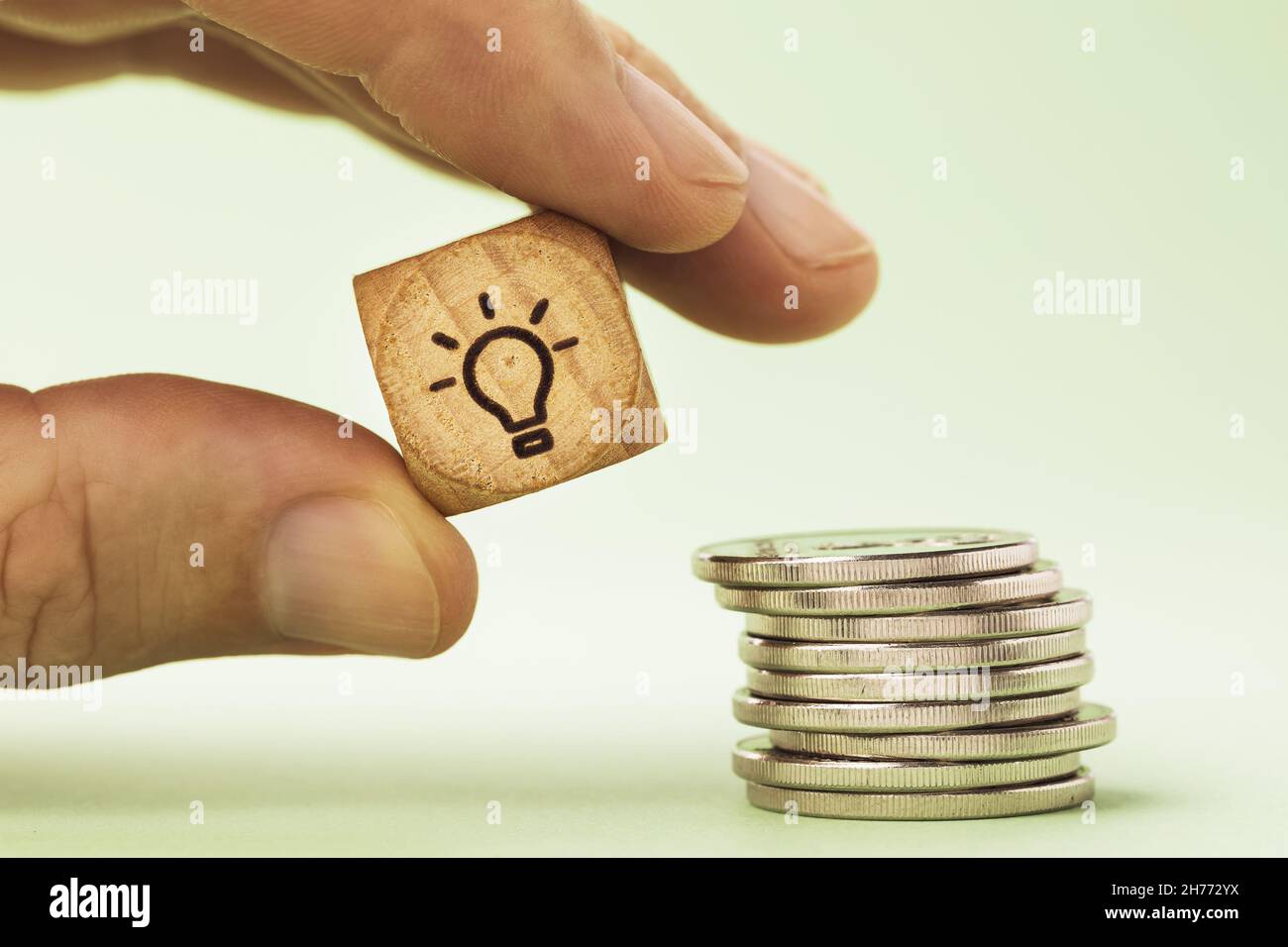 Un homme tient dans sa main un cube en bois avec une photo d'une ampoule près d'une pile de pièces de monnaie, un concept sur le sujet de l'économie d'énergie Banque D'Images