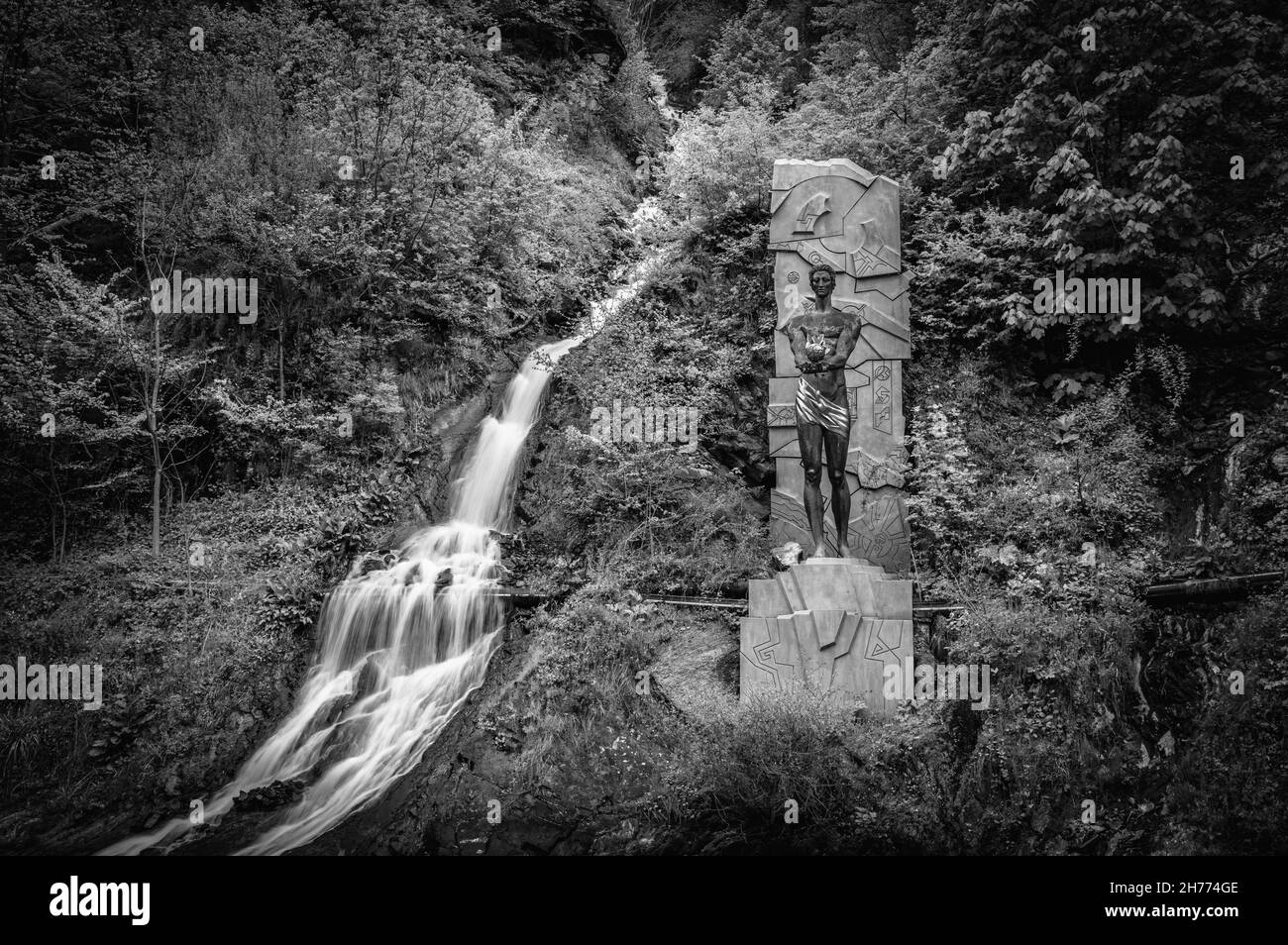 Ruisseau de montagne traversant les arbres et le monument à Prométhée dans la ville balnéaire de Borjomi, Géorgie.Noir et blanc. Banque D'Images
