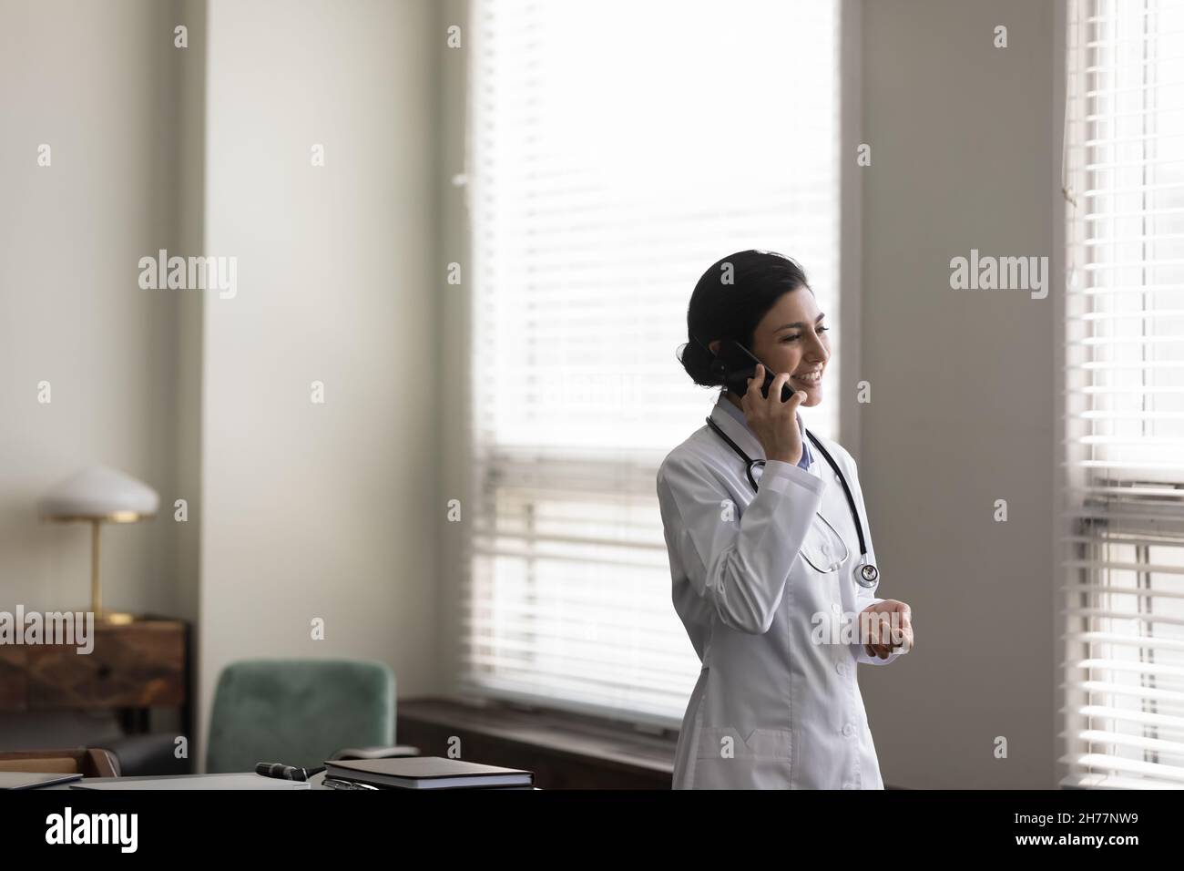 Femme indienne souriante médecin parlant au téléphone au bureau Banque D'Images
