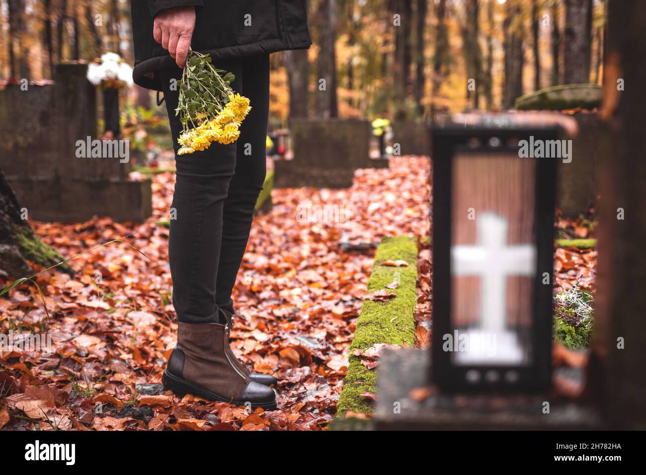 Deuil d'une femme tenant des fleurs entre les mains et debout à la tombe du cimetière.Tristesse et chagrin pendant les funérailles Banque D'Images