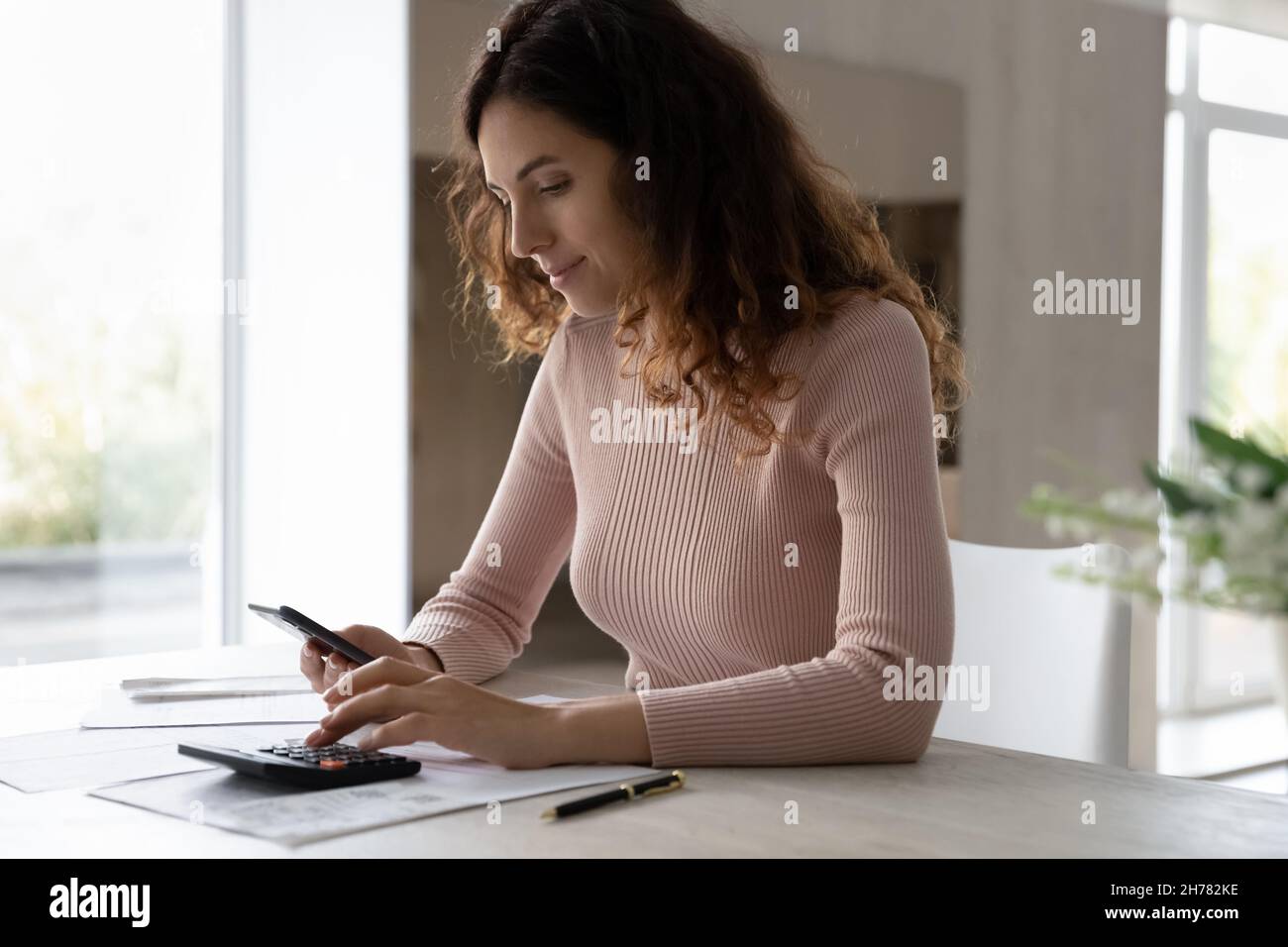 Jeune femme calculant les dépenses, payant les impôts, à l'aide d'un smartphone et d'une calculatrice Banque D'Images