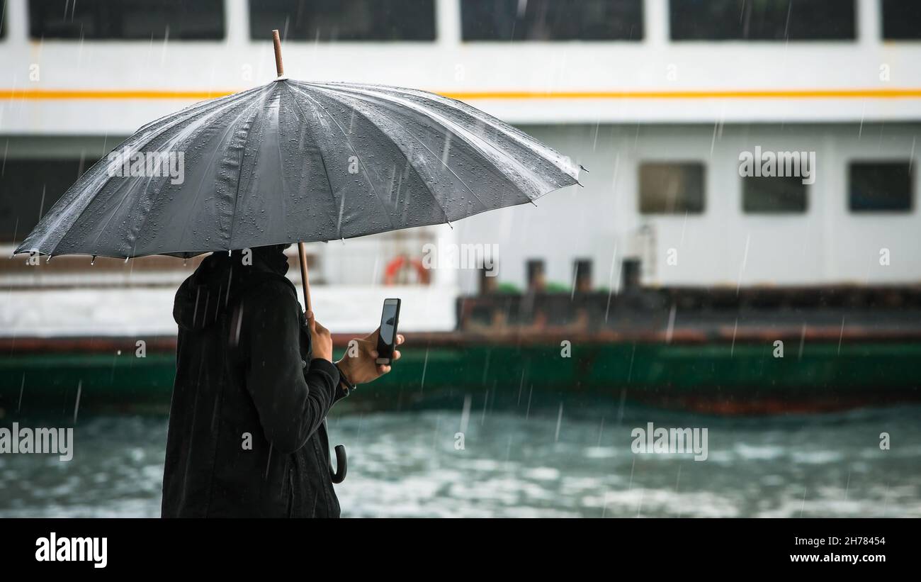 homme voyageur tenant son smartphone près de la mer par un jour de pluie Banque D'Images
