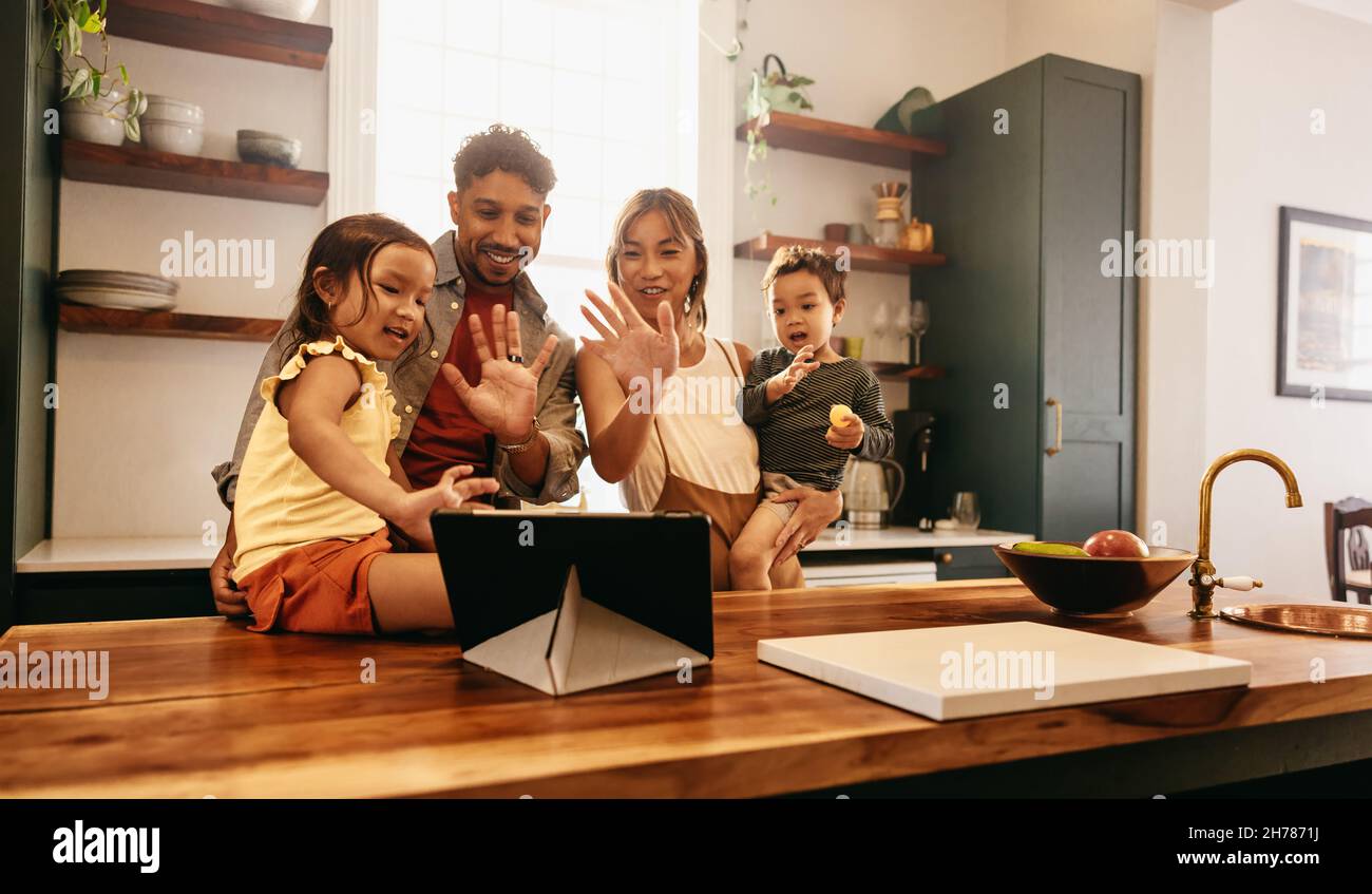 Une famille heureuse se faisant passer un appel vidéo sur une tablette numérique avec ses proches.Famille de quatre personnes souriantes tout en saluant leurs amis et Banque D'Images