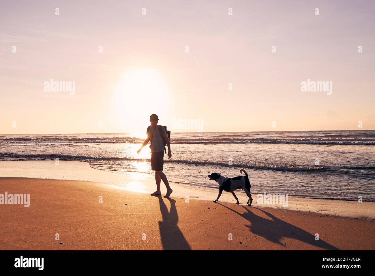 Silhouette de jeune homme pendant la marche avec un chien sur une plage de sable au beau lever du soleil.Copier l'espace sur le ciel. Banque D'Images