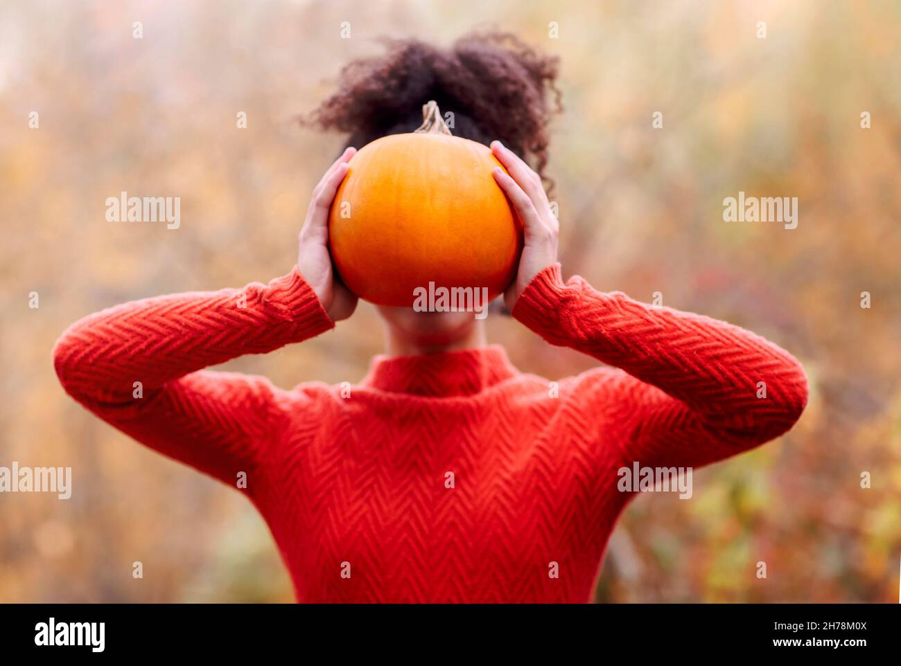 Jeune femme de race mixte avec des cheveux bouclés tenant la citrouille d'orange tout en se tenant contre un arrière-plan flou de forêt d'automne.Saison d'automne et concept de récolte Banque D'Images