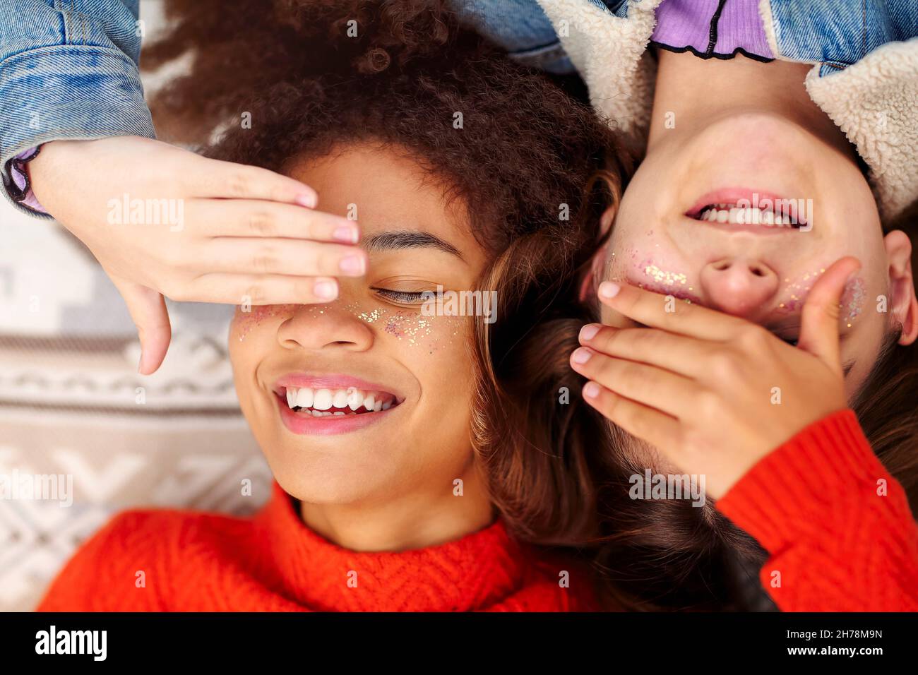 Vue de dessus de deux heureux multiracial adolescentes couvrant les yeux et souriant tout en étant allongé sur une couverture à l'extérieur, appréciant la jeunesse et la compagnie de chacun d'eux Banque D'Images