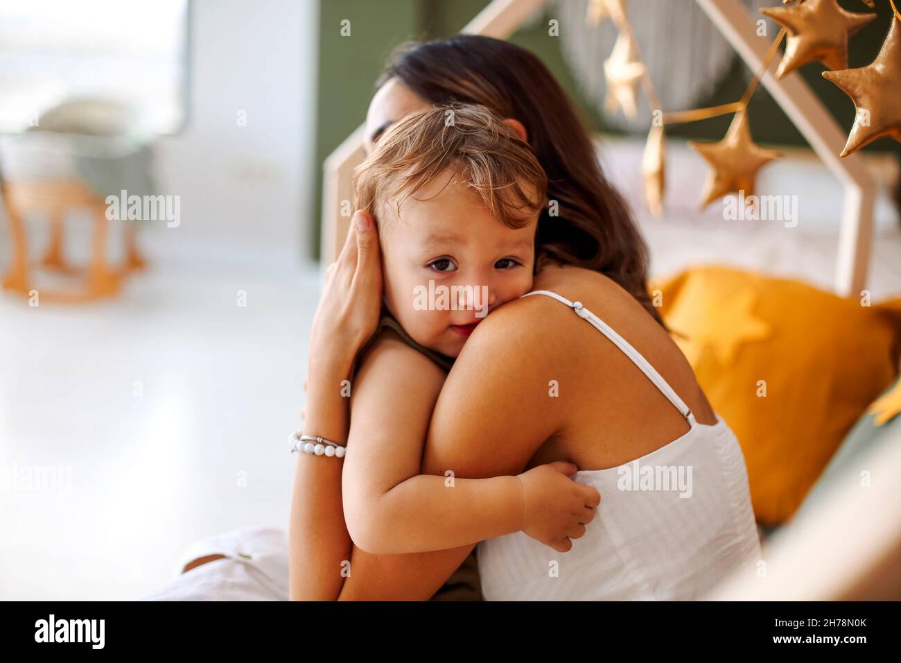 Jeune femme mère exprimant l'amour au petit bébé, assis sur le lit avec l'enfant endormi dans les mains et l'embrassant dans le front, photo tendre de l'état Banque D'Images