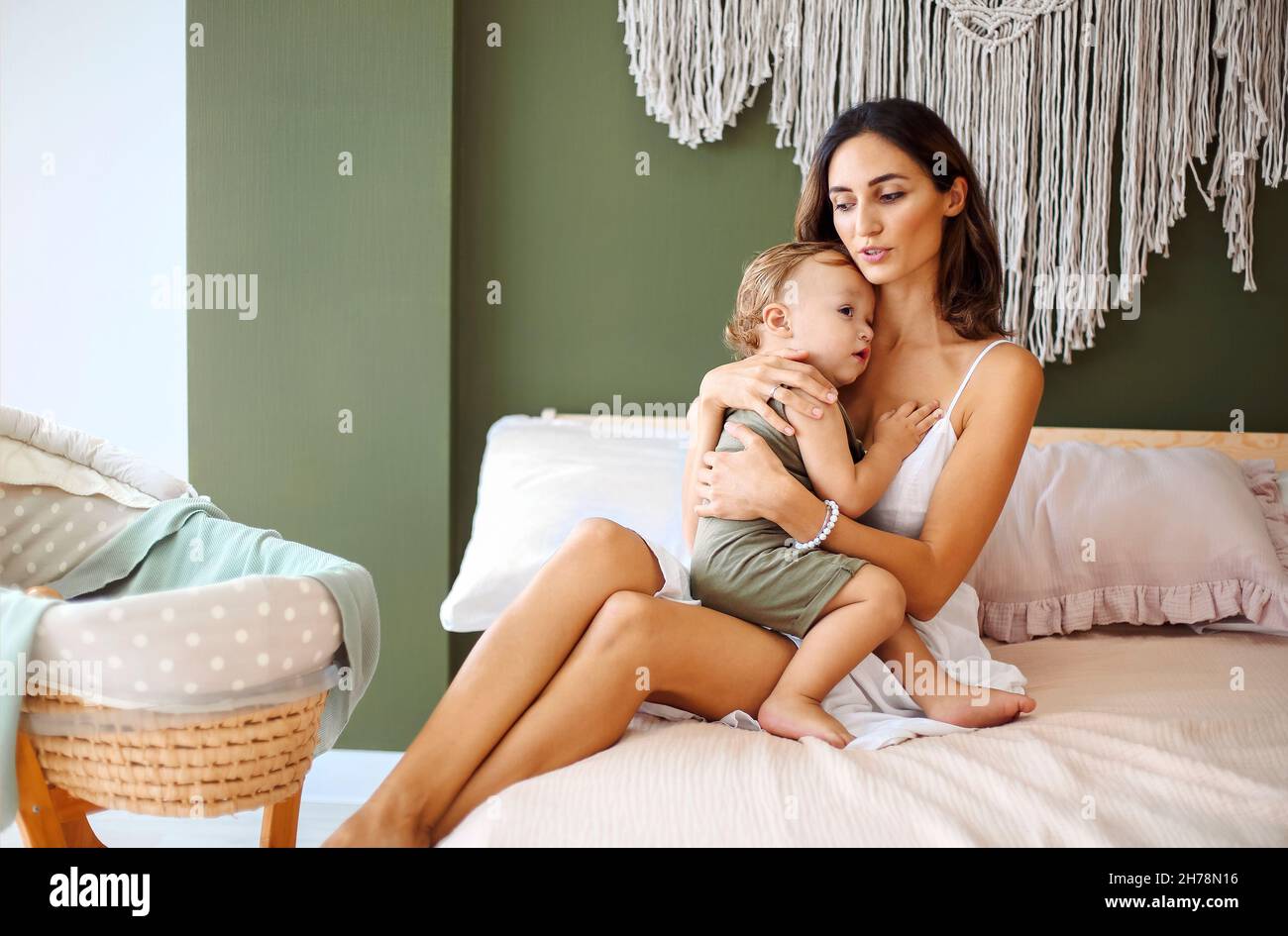 Jeune femme mère exprimant l'amour au petit bébé, assis sur le lit avec l'enfant endormi dans les mains et l'embrassant dans le front, photo tendre de l'état Banque D'Images