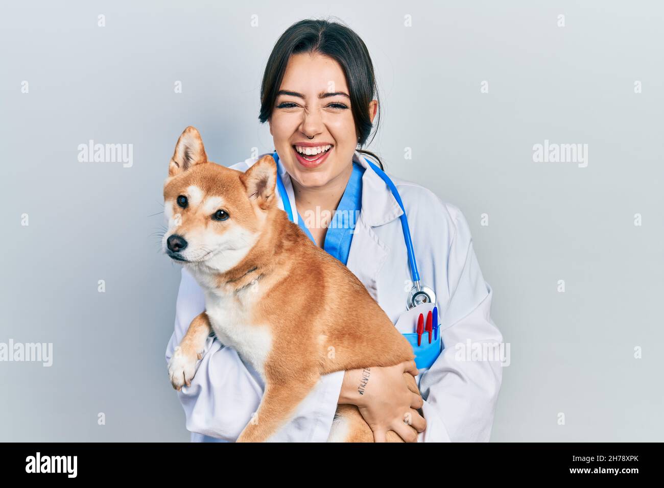Belle femme vétérinaire hispanique tenant le chien souriant et riant dur dehors fort parce que drôle de blague folle. Banque D'Images