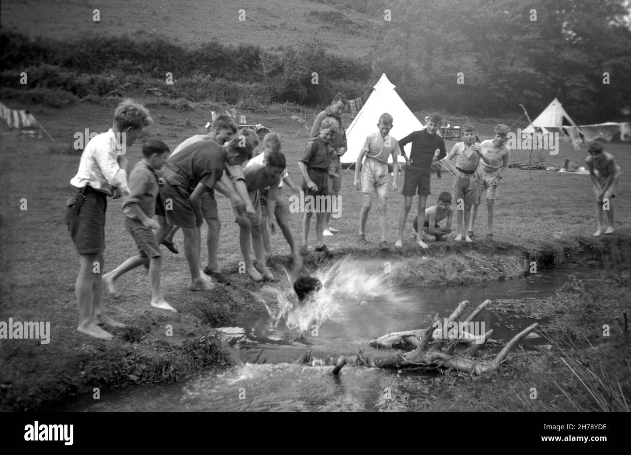 1939, historique, camp de scouts d'été, Ringmore, Devon,Angleterre, Royaume-Uni, à l'extérieur dans un champ surveillé par d'autres scouts de cub, un garçon faisant une splash alors qu'il prend un plongeon dans le ruisseau. Banque D'Images