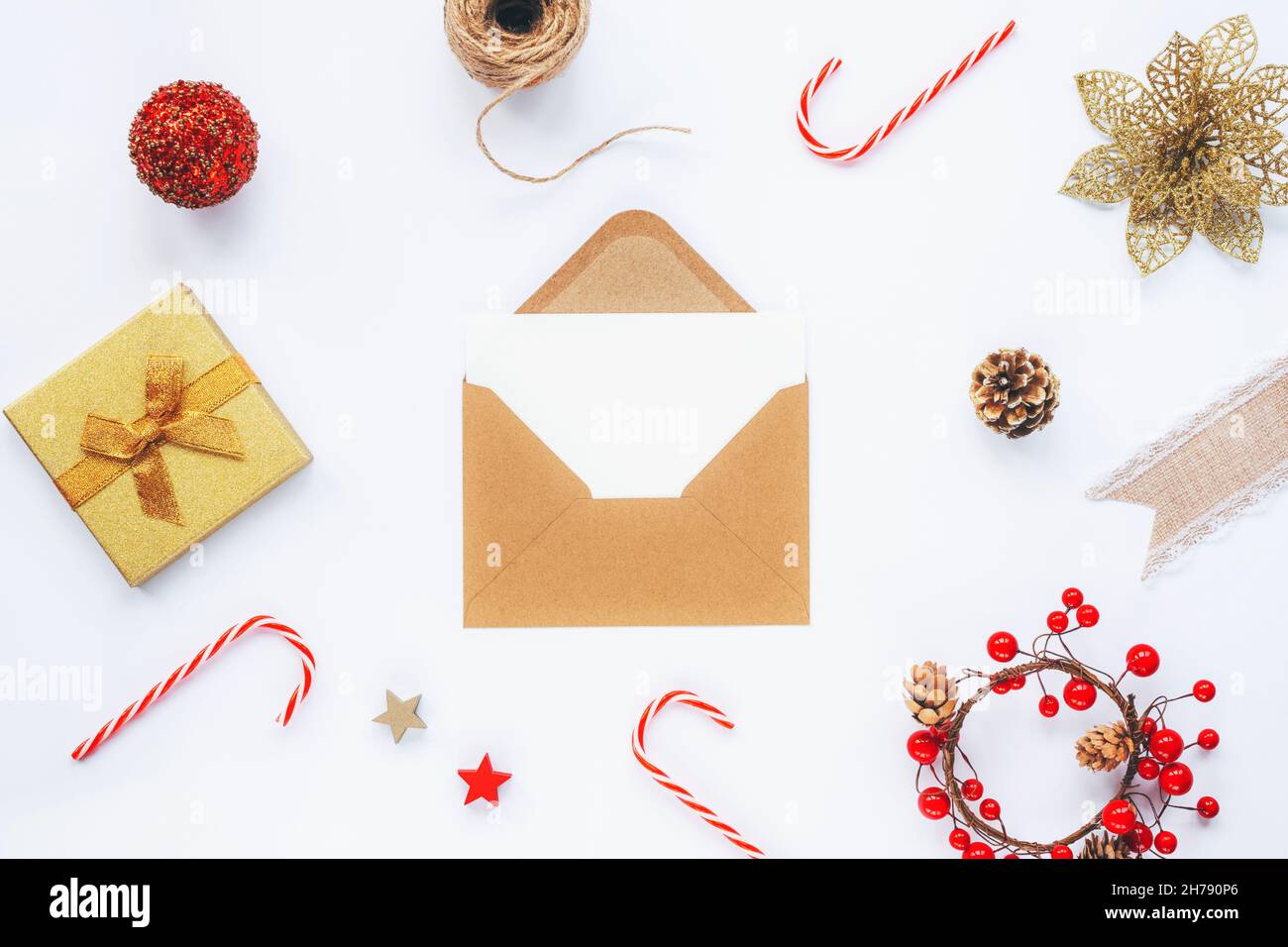 Enveloppe brune ouverte avec carte blanche vierge et décorations de Noël,  Cannes de bonbons et boîte-cadeau sur fond de table blanc.Vue de dessus,  plan de travail, bac de copie Photo Stock -