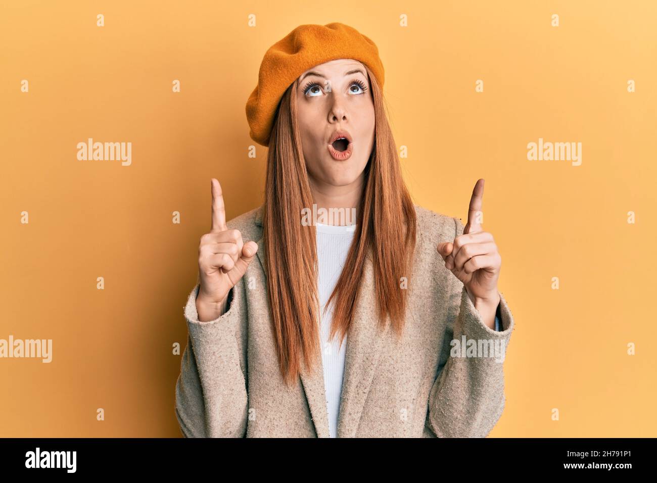 Jeune femme irlandaise portant le regard français avec beret stupéfait et surpris regardant vers le haut et pointant avec les doigts et les bras relevés. Banque D'Images