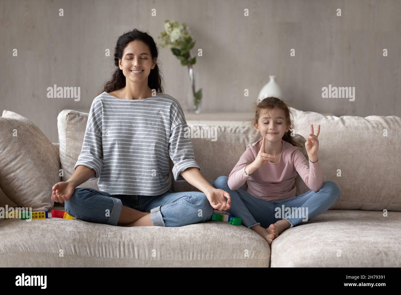 Mère heureuse et petite fille pratiquant le yoga, méditant sur le canapé Banque D'Images