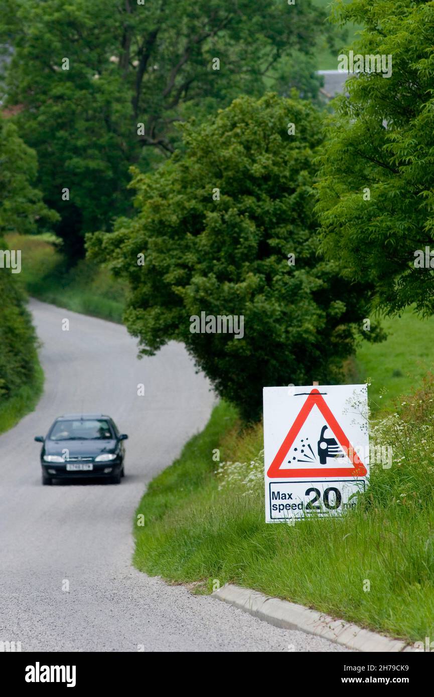 Une voiture de tourisme passe un panneau de vitesse maximale de 20 km/h sur une route de pays B recouverte de copeaux de pierre frais, Leicestershire, Angleterre, Royaume-Uni. Banque D'Images