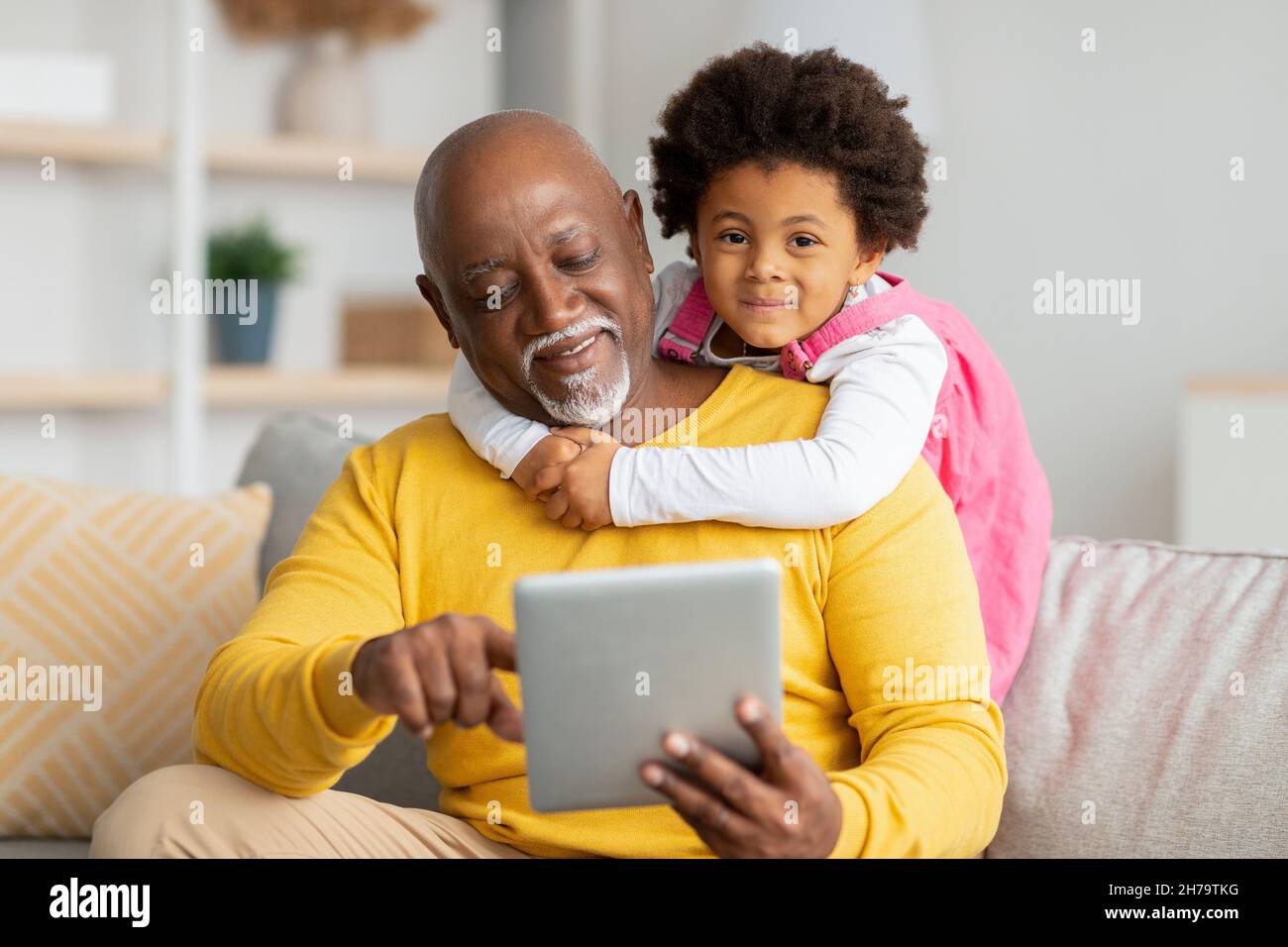 Happy african american preschooler girl hugs homme mature surf dans Internet ou jouer à un jeu en ligne sur tablette Banque D'Images
