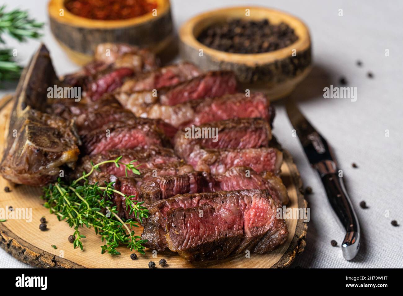 Steak de bœuf grillé moyen rare coupé en tranches sur une planche à découper en bois avec épices Banque D'Images