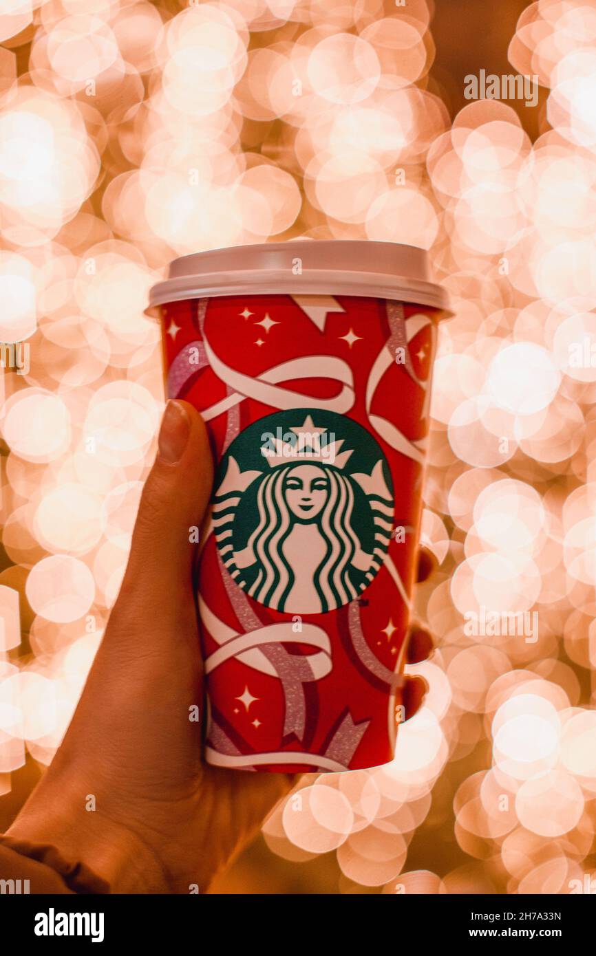 Main féminine tenant une tasse de café Starbucks du nouvel an sur un fond de lumières de bokeh de Noël dorées Banque D'Images