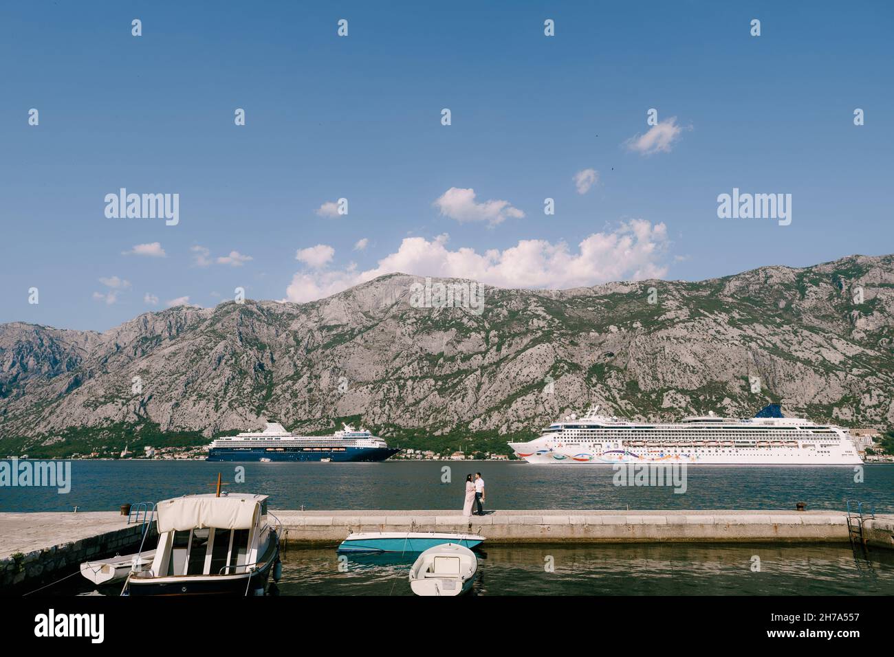 Mariée et marié se tiennent sur la jetée sur fond de bateaux de croisière et de montagnes Banque D'Images