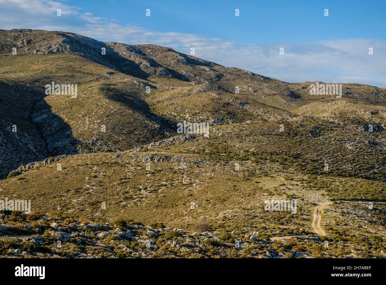Paysage avec de minuscules gens qui font de la randonnée sur une piste lointaine au-dessus d'un terrain de montagne accidenté, Benimaurell, province d'Alicante, Espagne Banque D'Images