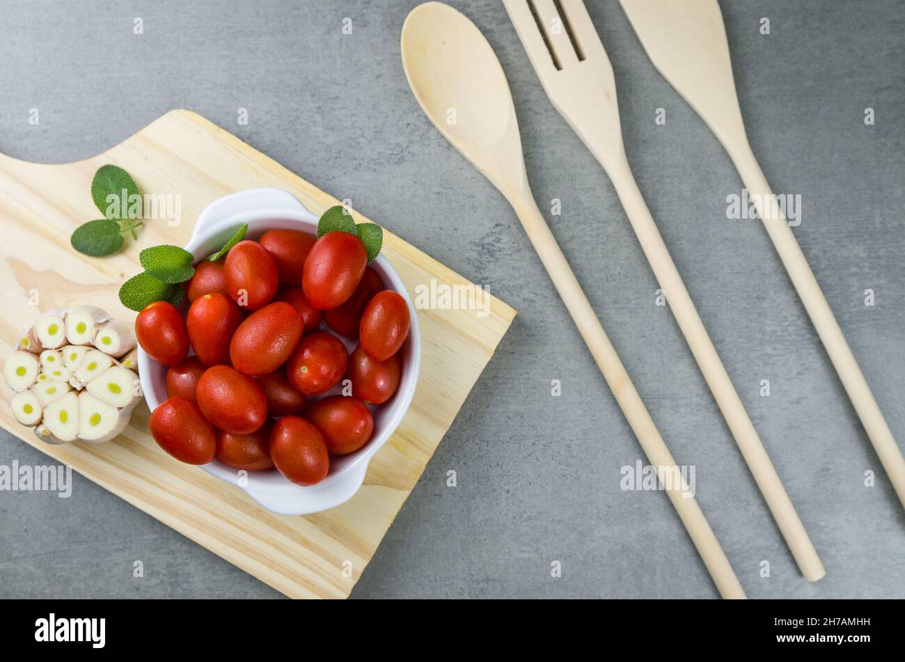 Panneau en bois avec tomates cerises sur fond gris. Fond culinaire. Banque D'Images