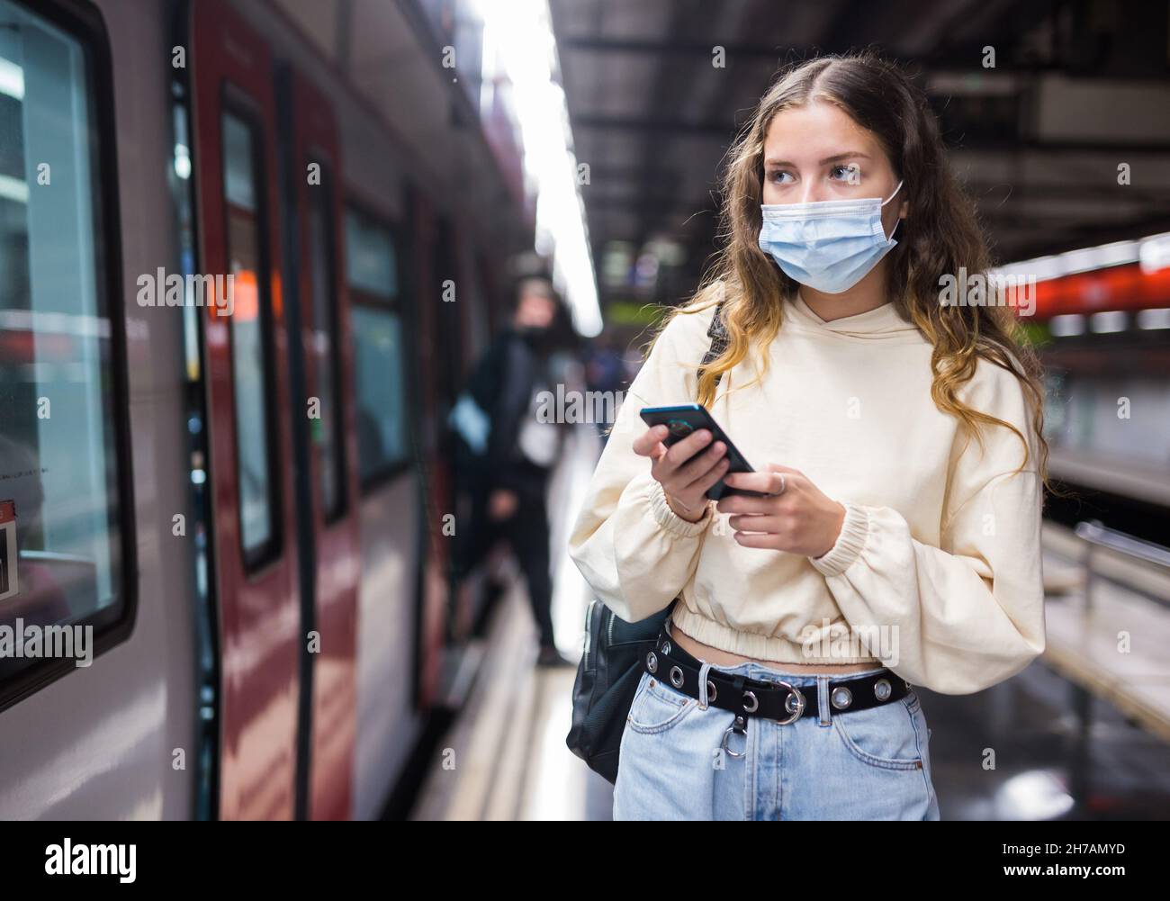 Jeune femme au masque en utilisant un téléphone portable en attendant le métro Banque D'Images