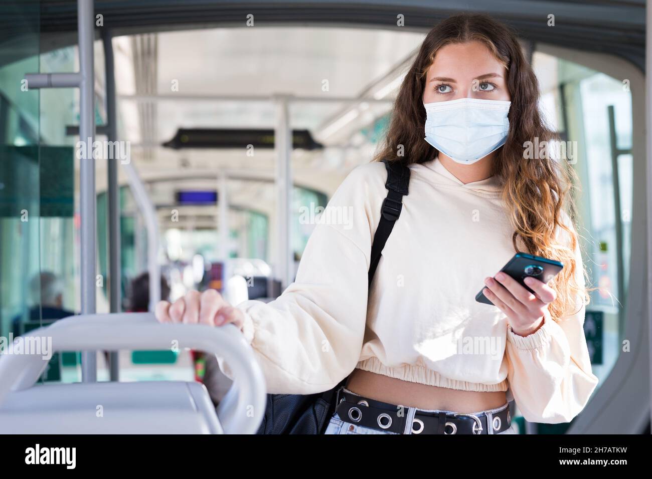 Femme en masque utilisant un téléphone portable sur le chemin de travail en tram Banque D'Images