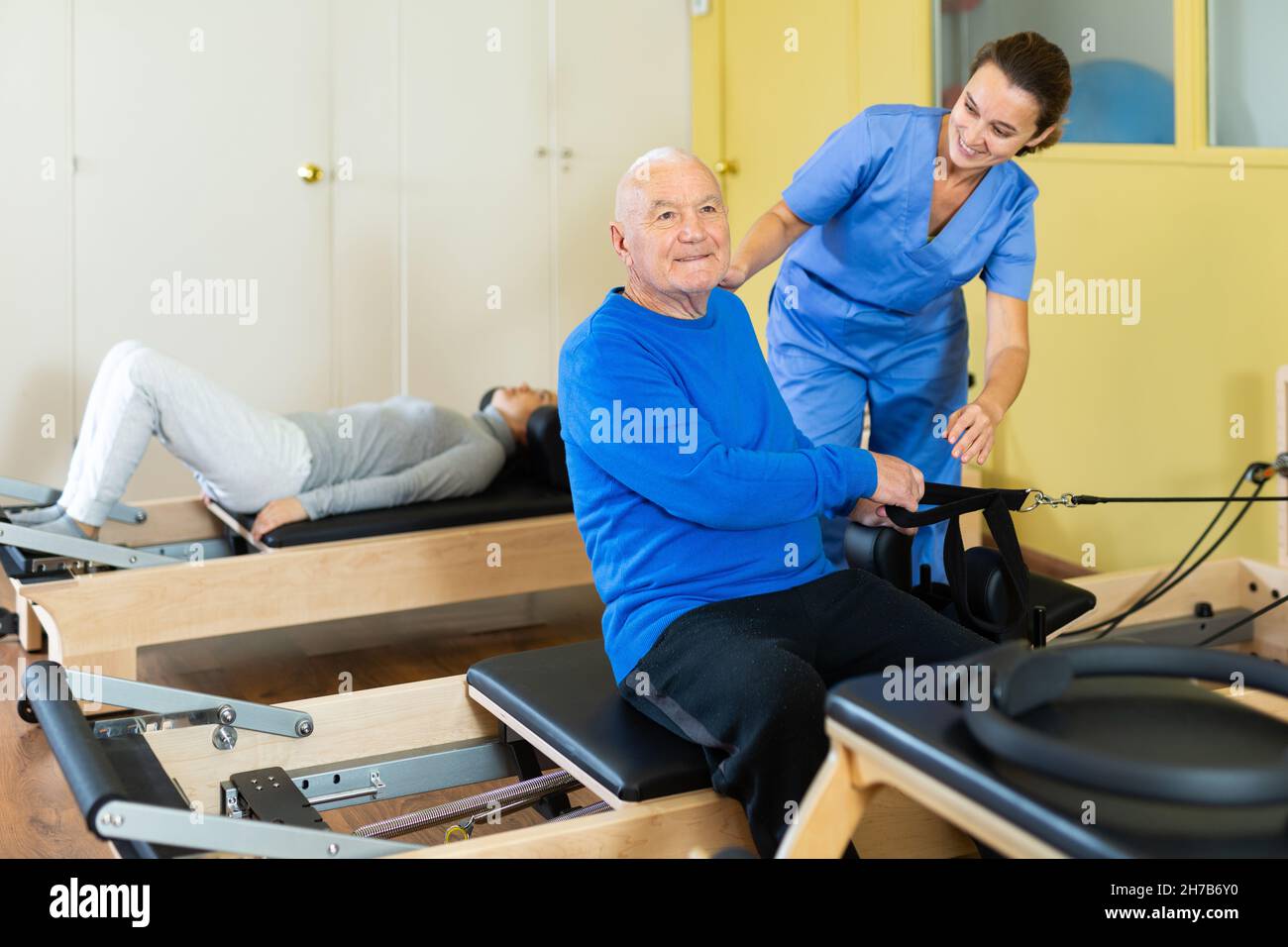 Femme physiatre aidant l'homme âgé faisant des exercices sur le réformateur Banque D'Images
