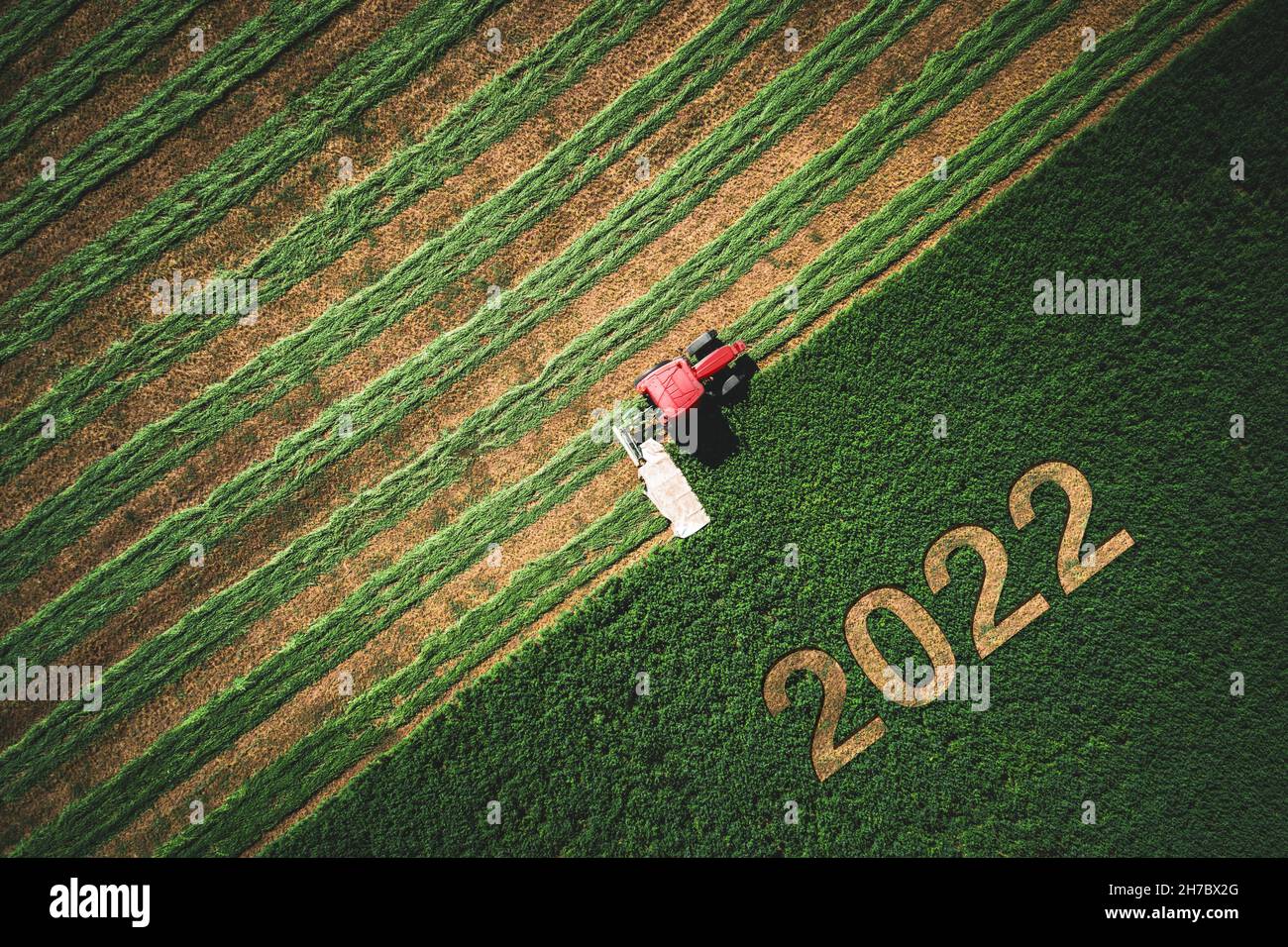 2022 concept Happy Ney Wear et tracteur rouge fauchant le champ vert. Banque D'Images