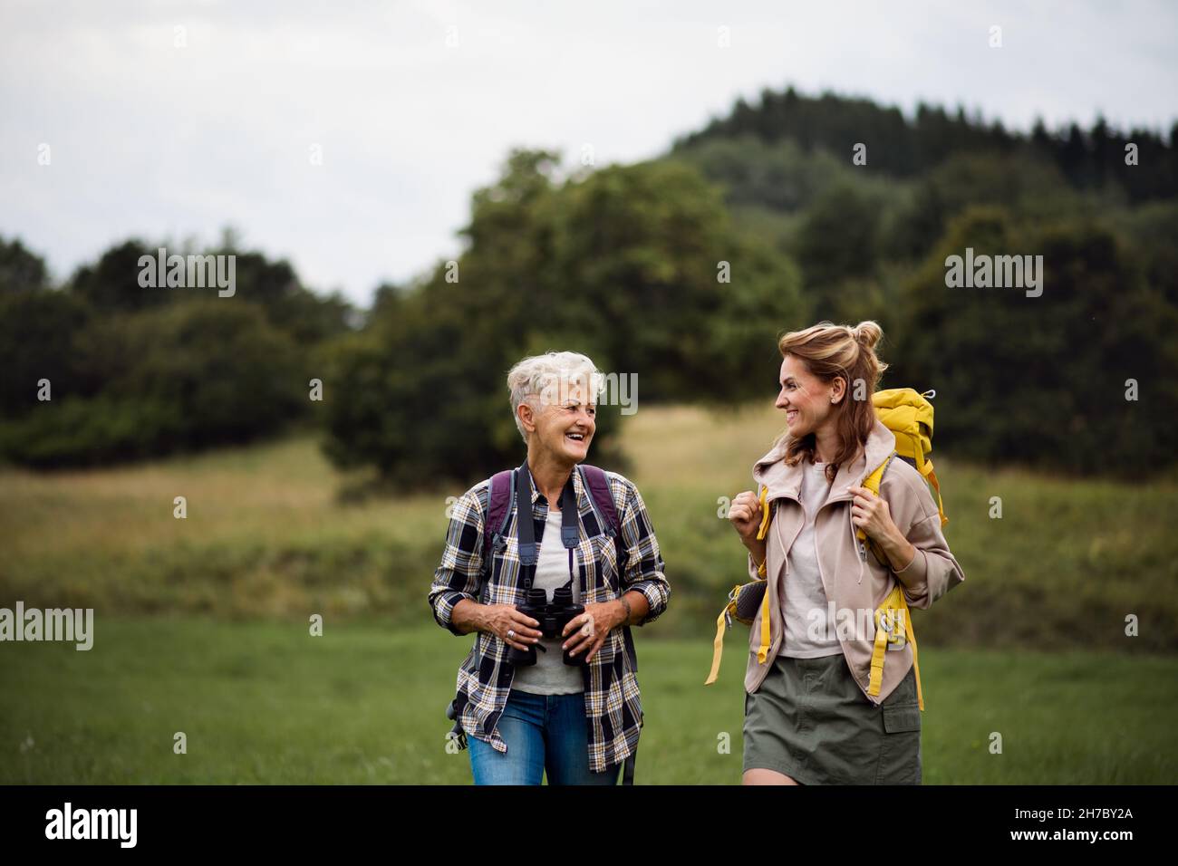 Femme âgée active avec des jumelles en randonnée avec sa fille adulte à l'extérieur dans la nature. Banque D'Images