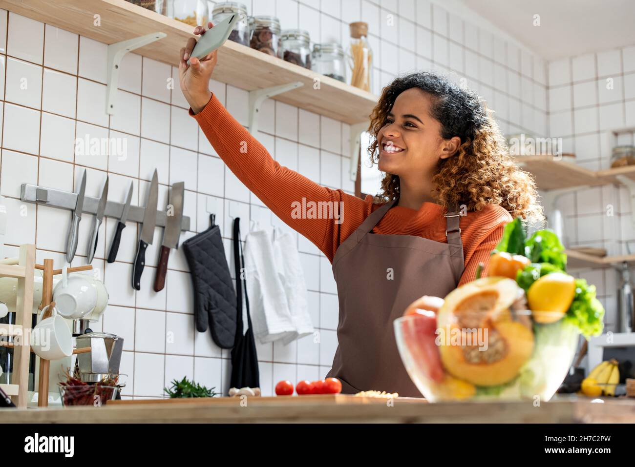 Portrait d'une jeune femme afro-américaine souriante prenant le selfie avec un smartphone tout en cuisinant dans la cuisine à la maison Banque D'Images