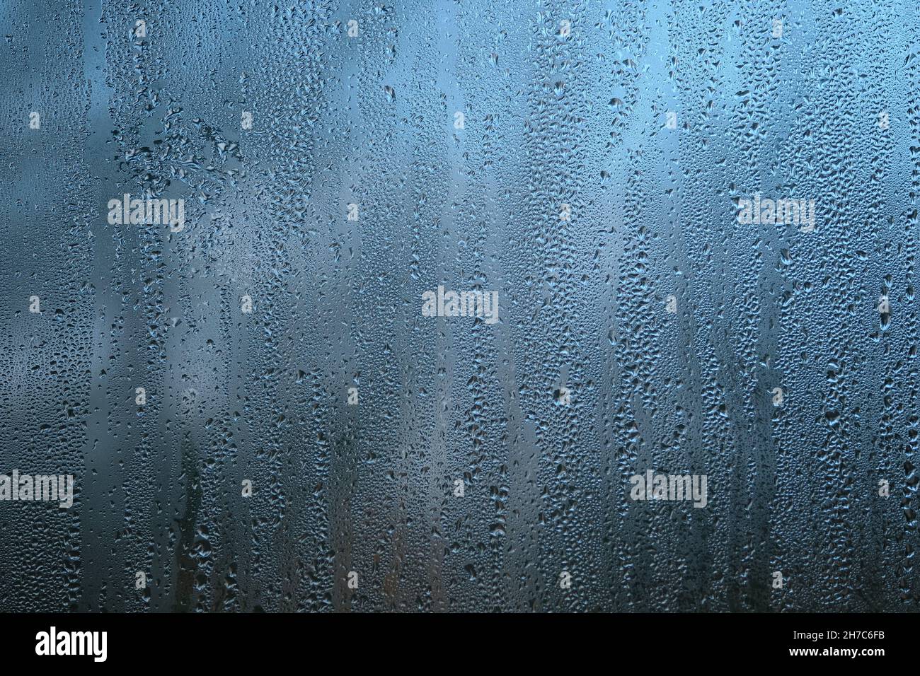Arrière-plan avec des gouttes de pluie sur le verre de la fenêtre le jour sombre de l'automne sur fond bleu flou gros plan Banque D'Images