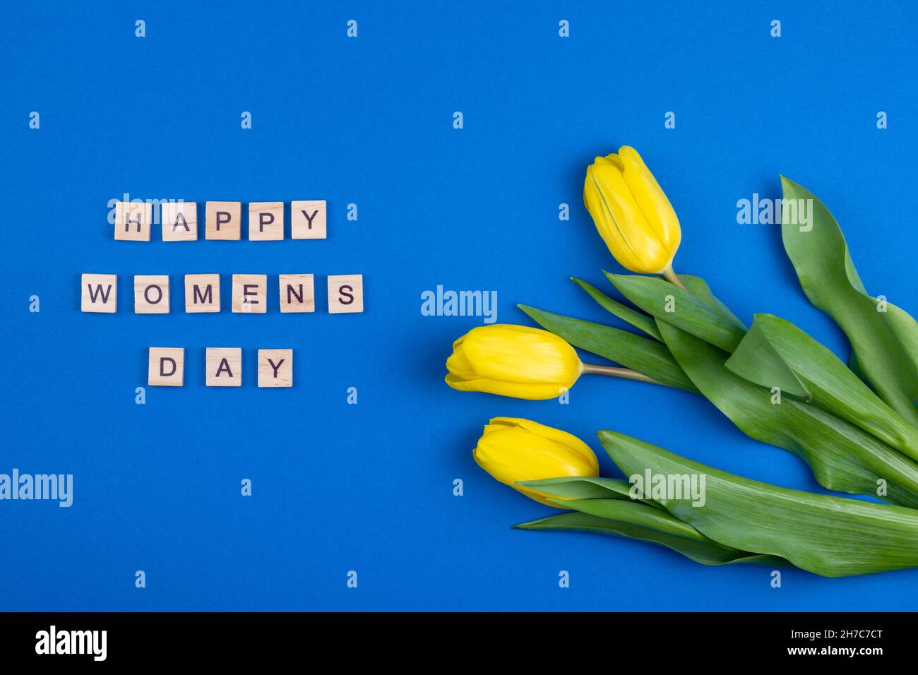 Carte de fête des femmes.Lettres en bois.Trois tulipes jaunes de printemps fleurs.Arrière-plan avec fleurs tulipes gros plan.Cadeau.Arrière-plan bleu.Bouquet simple. Banque D'Images