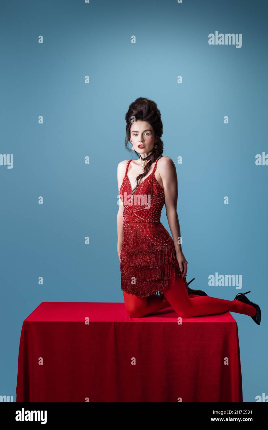 Portrait d'une jeune adorable femme en rouge foncé, robe de soirée couleur  vin posé sur une table avec un tissu rouge isolé sur fond bleu Photo Stock  - Alamy