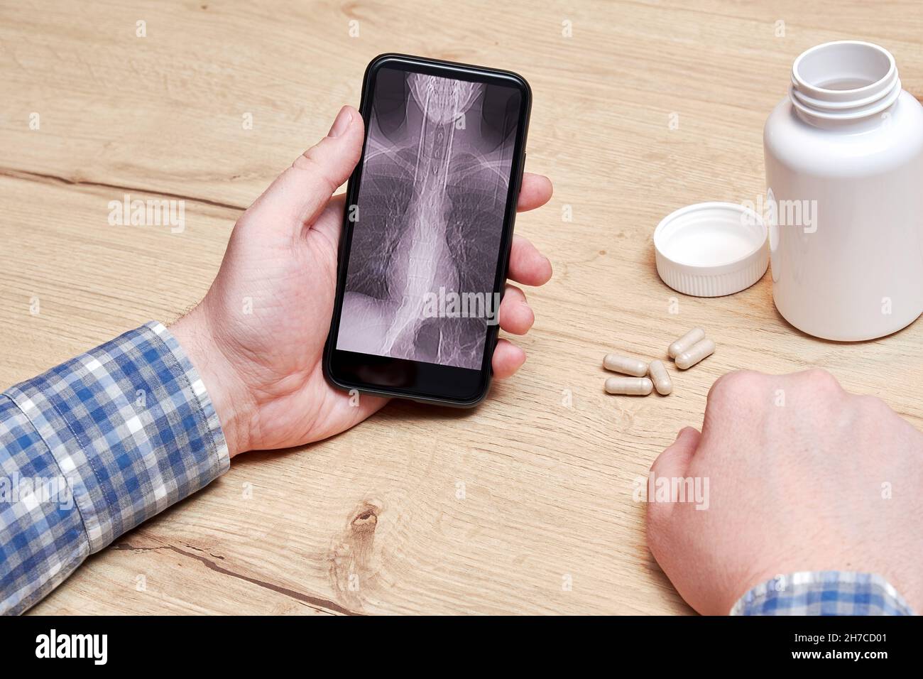 Homme assis avec un téléphone et regardant une tomodensitométrie de ses poumons.Diagnostic de pneumonie et de maladie.Pilules et flacons médicaux Banque D'Images
