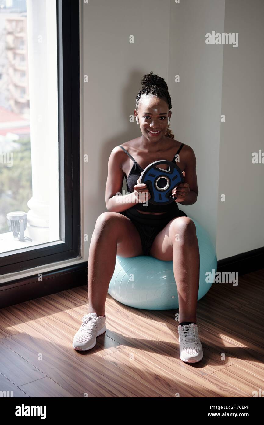 Souriante jolie jeune femme faisant la torsion russe sur le ballon de fitness avec le poids lourd dans les mains Banque D'Images
