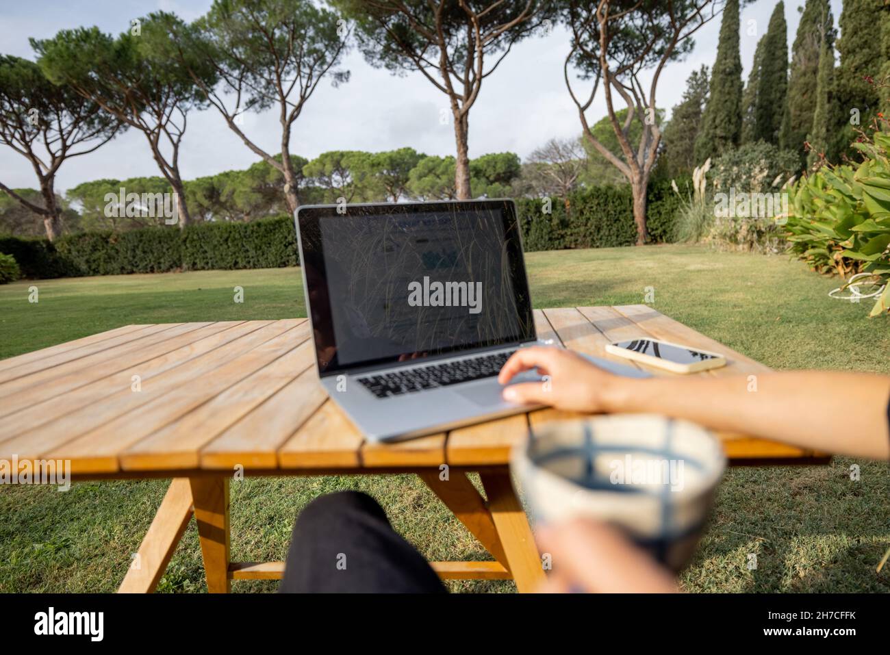 Une femme utilise un ordinateur portable et boit du thé à la table sur la pelouse Banque D'Images