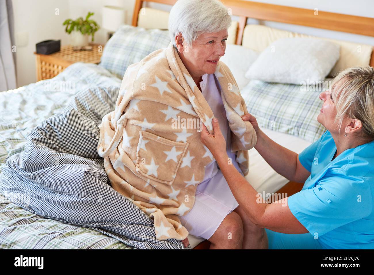 La femme du service de soins infirmiers aide la vieille femme à mettre un peignoir à la maison ou dans la maison de retraite Banque D'Images