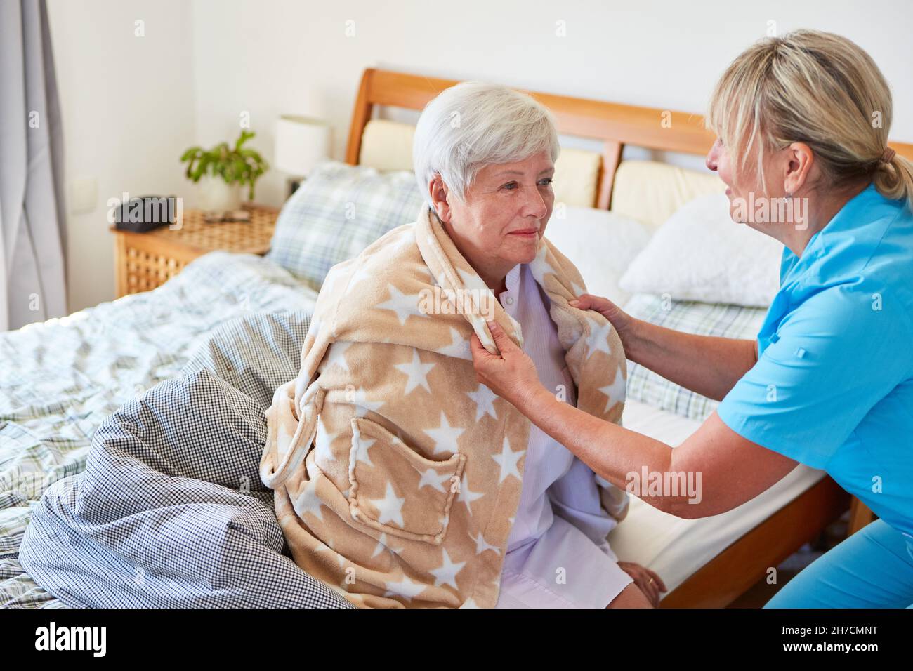 Une travailleuse de soins aux personnes âgées aide une femme âgée malade à mettre un peignoir dans la maison de retraite ou à la maison Banque D'Images