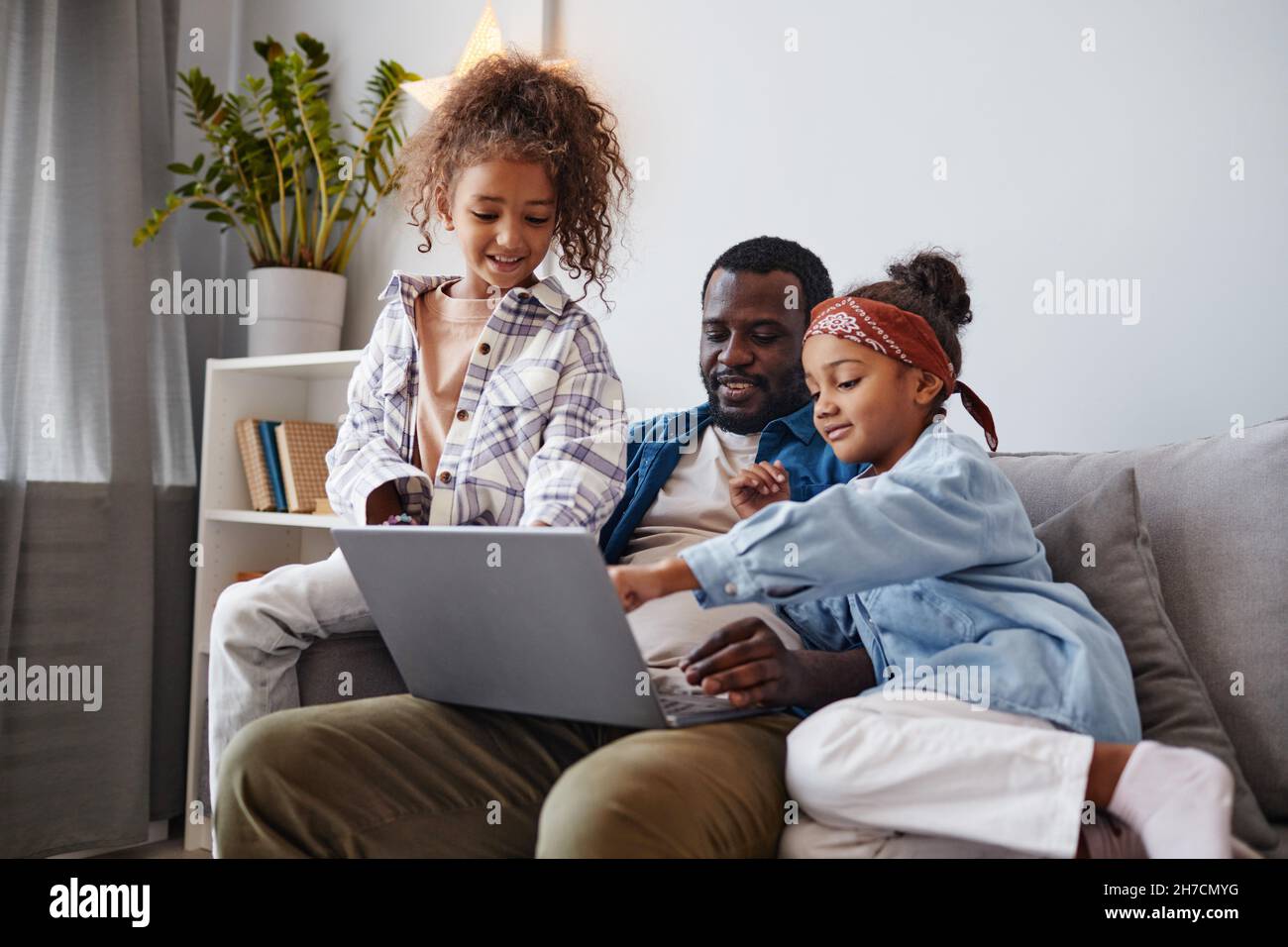 Portrait d'un père afro-américain souriant utilisant un ordinateur portable avec deux filles, espace de copie Banque D'Images