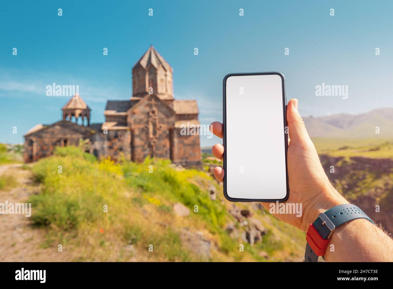 La main du voyageur tient un smartphone avec un écran vierge sur le fond d'une ancienne église arménienne.Concept d'application mobile pour touris Banque D'Images