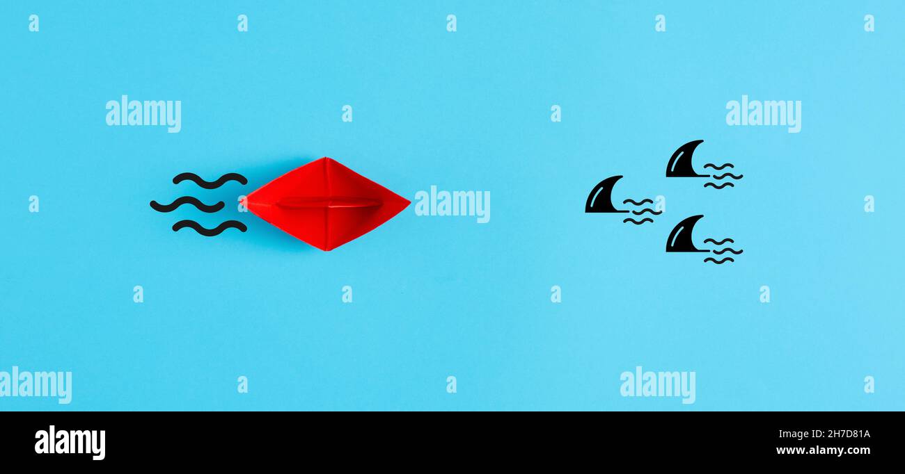 Concept de danger, de risque, de menace ou d'assurance.Le bateau à papier rouge se déplace vers un groupe de requins sur fond bleu. Banque D'Images