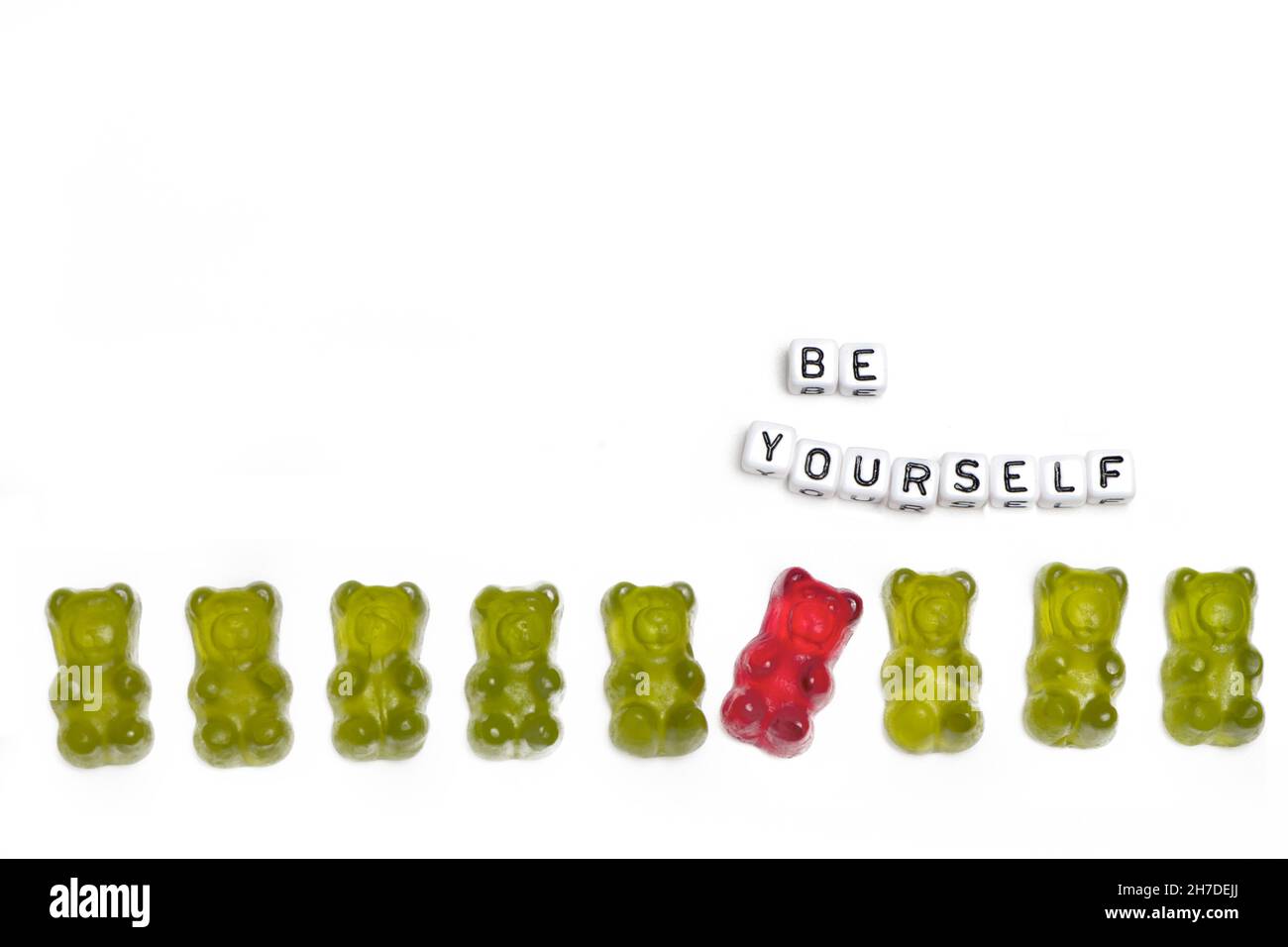 une rangée d'ours verts délicieux dans laquelle un gars rouge se comporte différemment par rapport à un concept d'individualité et d'être différent est isolée sur un dos blanc Banque D'Images