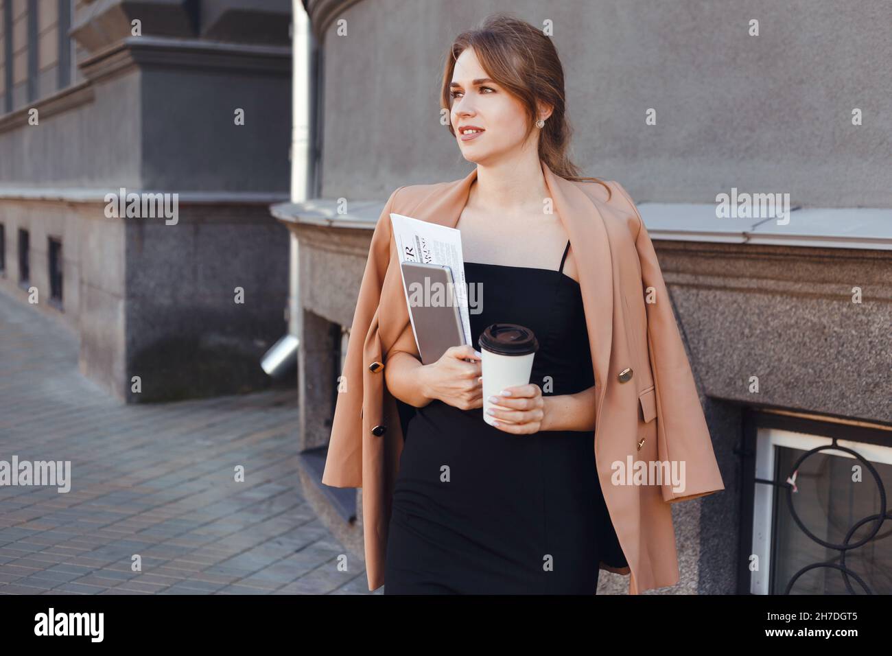 Femme d'affaires pressée avec un café à emporter, une tablette numérique et des documents qui marchent dans la rue le matin Banque D'Images