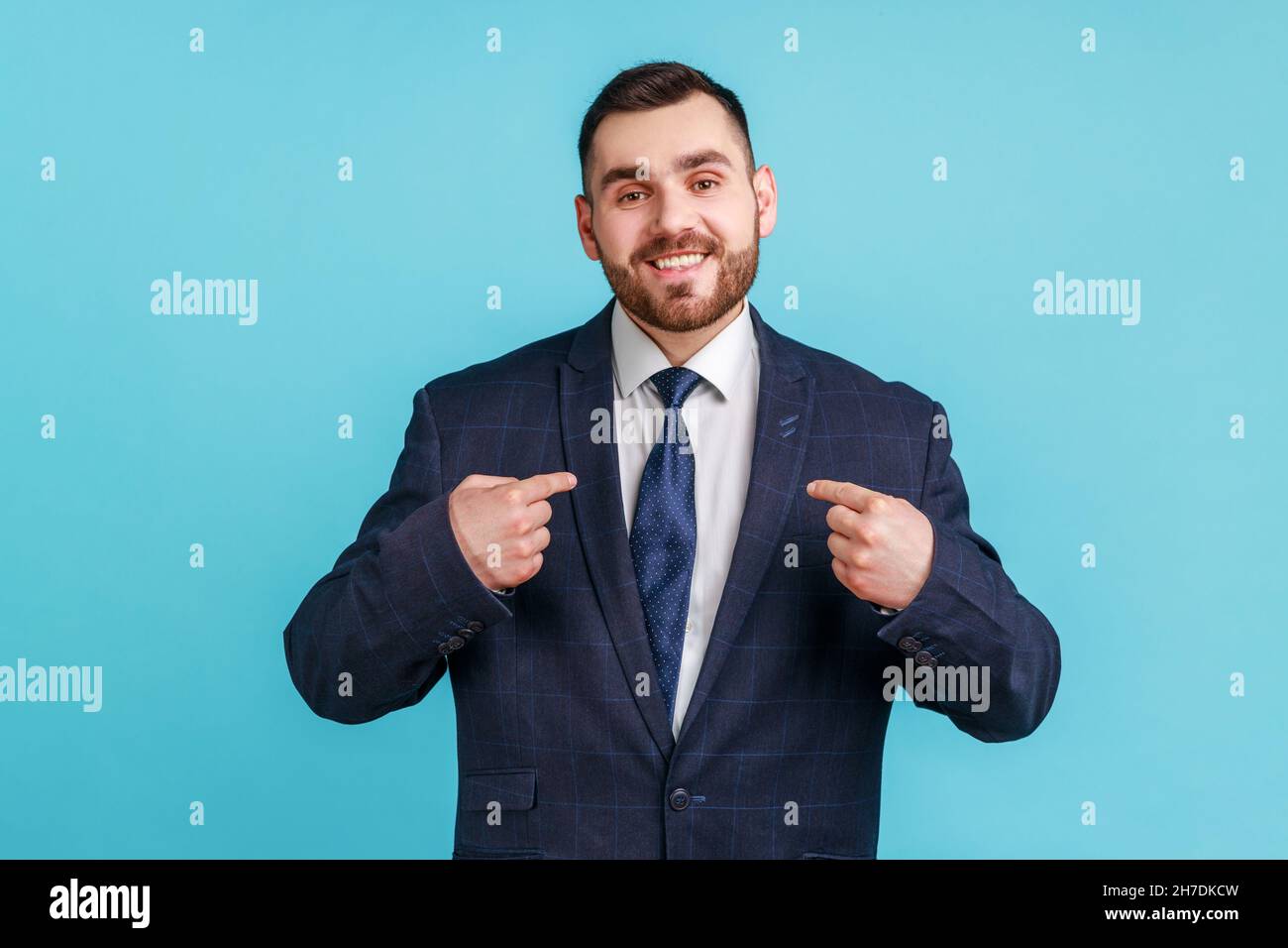 C’est moi.Jeune homme ambitieux avec barbe portant un costume de style officiel avec un sourire éclatant sur le visage pointant des doigts sur lui-même, homme d'affaires confiant.Studio d'intérieur isolé sur fond bleu. Banque D'Images
