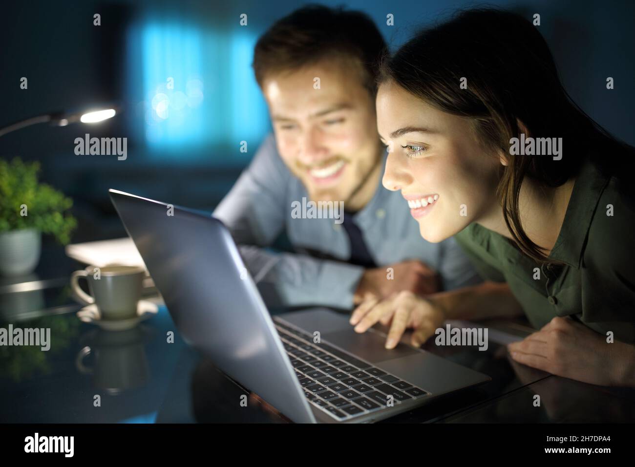 Couple heureux de regarder du contenu sur un ordinateur portable dans la nuit à la maison Banque D'Images