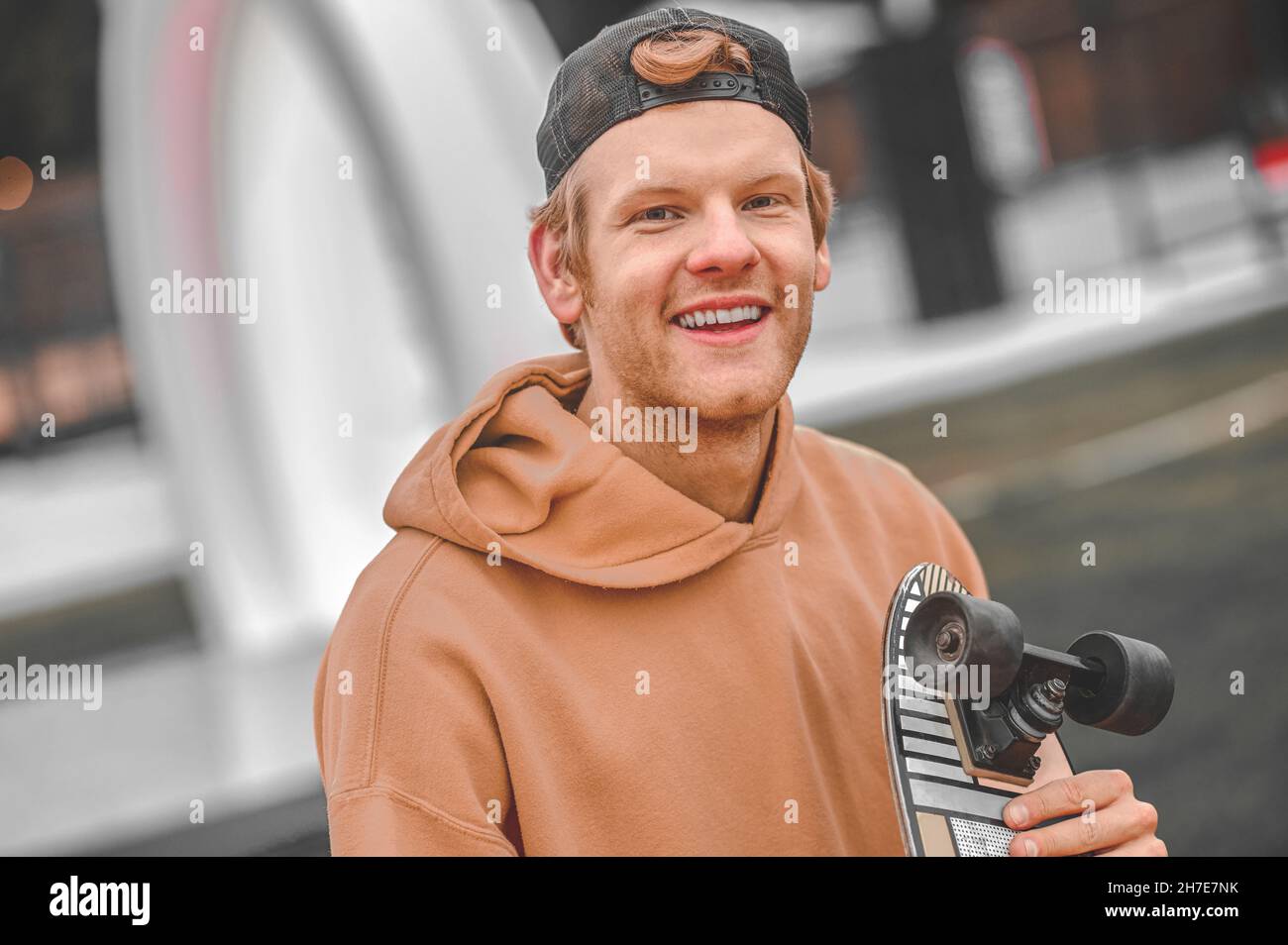 Sympathique homme souriant avec un skateboard regardant un appareil photo Banque D'Images