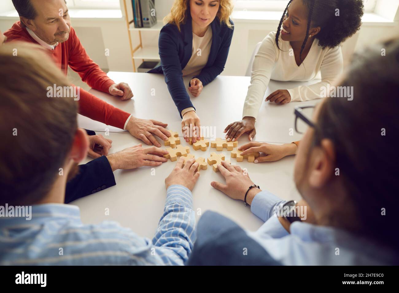 Bonne équipe d'affaires diversifiée assis autour de la table de bureau et joignant des pièces de puzzle Banque D'Images