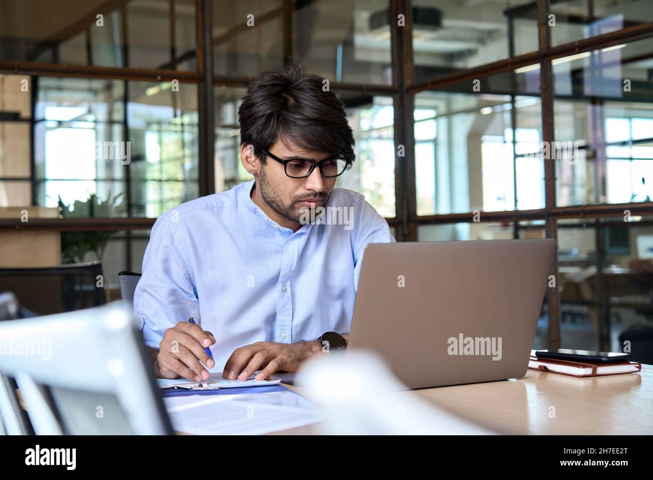 Un jeune homme d'affaires indien regarde un webinaire sur un ordinateur portable au bureau. Banque D'Images